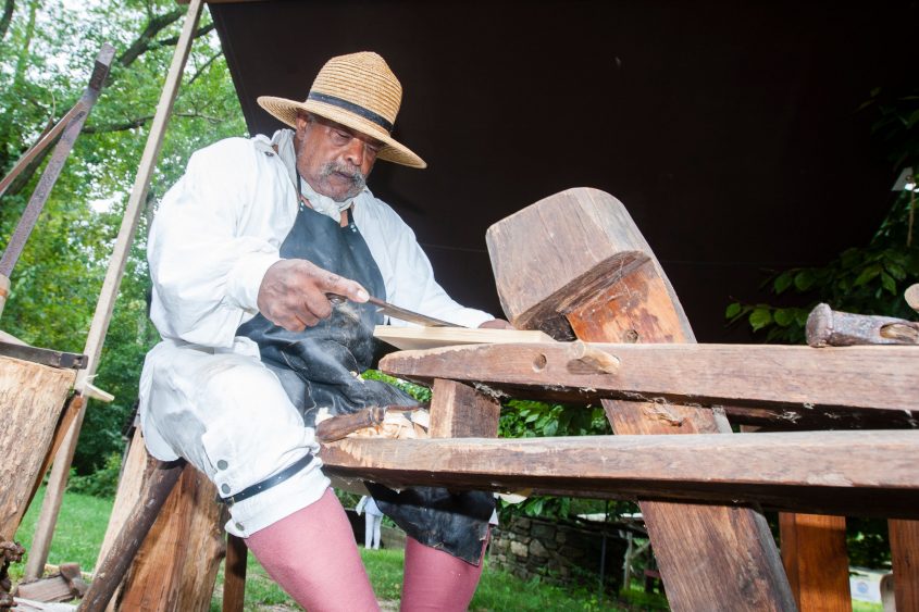 Man in colonial dress using a drawknife
