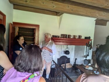 A group of four teachers are standing in a historic kitchen, speaking with a Museum Educator dressed in colonial clothing 